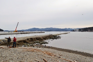 海岸から湾の奥へ伸びる護岸と、クレーンや工事中の構造物が見える静かな海の写真