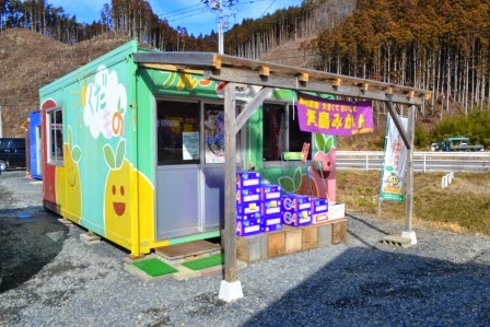 山林に囲まれた敷地内に、店先に果物の箱が積まれている、果物のイラストが描かれたカラフルな外壁の店舗の写真