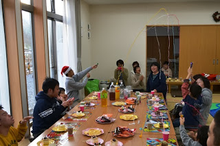 長いテーブルに料理や飲み物が並び、クラッカーを飛ばして子どもも大人も盛り上がっている写真