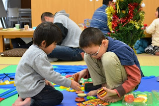 子どもが二人でマットの上に座り、ハンバーガーのおもちゃなどで仲良く遊んでいる写真