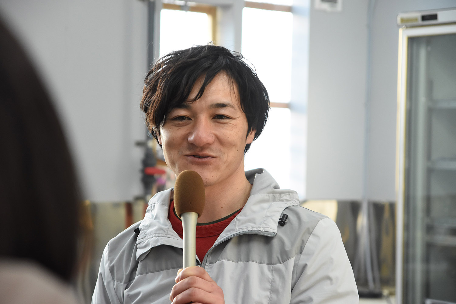 リポーターの女性と向かい合って座った高橋さんが、マイクを持って笑顔で話をしている写真