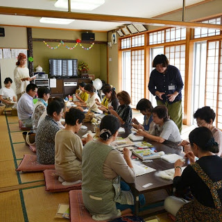 2間続きの和室にテーブルが並び、座布団に座った多くの女性たちが、羊毛フェルトでウサギを作っている様子を写した写真