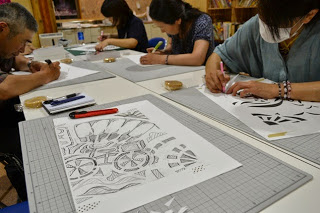 長机の上で複数の参加者がカッターを使いながら切り絵の作業を集中して行っている様子の写真