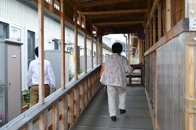 仮設住宅の外廊下を、弁当を配達するために歩いている女性の後ろ姿を写した写真