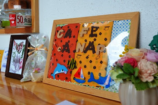 店名の文字とイルカやヨットが描かれたカラフルな手作り看板と、花飾りがカウンターに飾られている、店内の装飾の写真