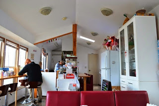 窓際のカウンター席に男性が座って作業をし、手前に赤いソファとレジカウンターが見える、木の温もりを感じる店内の様子を示した写真