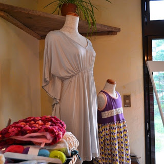 店内のマネキンに着せられたグレーのワンピースと子ども用の紫色の柄入りのワンピースの横に、毛糸の帽子や衣類が並んでいる写真