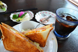 クロックムッシュと小鉢の料理、アイスコーヒーが木製のテーブルに並べられた、手作り感あふれる料理の写真