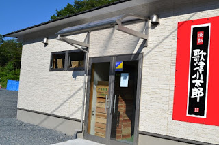 白い外壁に赤い看板が掲げられた「歌津小太郎」と書かれた加工場の外観写真