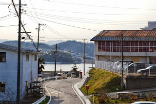 S字型に曲がりくねった道が通っている左側に白い2階建ての家屋が建っている写真