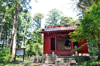 森の中に赤い外壁の小さな神社が建っていて、左手に説明看板が立っている神社の外観写真