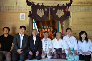 拝殿内の神棚の前で、正座して並ぶ7人の男女が和服やスーツを着て笑顔で写っている写真