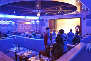 青い照明に照らされた会場で人々がテーブルに座って談笑している写真