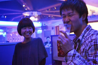 青い照明の会場で、飲み物を飲む男性と隣で笑顔の女性が楽しそうにしている写真