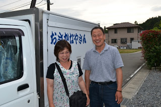 移動販売する軽トラックの横で、仲の良さそうな及川さんご夫婦が笑顔で並んで立っている様子の写真