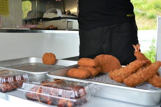 移動販売車のカウンターに、エビフライやコロッケなどの揚げたての食品が銀のトレーに乗せられている写真