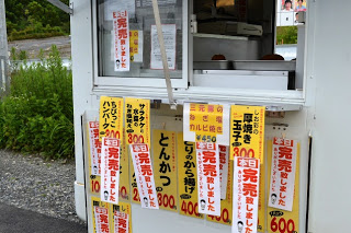異動販売車の販売窓に「とんかつ」「ハンバーグ」「玉子焼き」などのメニューと値段が黄色と赤の紙に書かれてたくさん貼られており、いくつかは「完売しました」と書かれている写真。