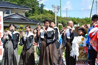 笛を持った演奏者たちが並んで立ち、真剣な表情で音を合わせて演奏している写真