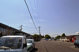 左側に仮設住宅が並び、車が駐車している広いアスファルトの道が、奥まで続いている写真