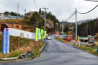 舗装された坂道の右側に複数の建設車両が停まっている、宅地造成地の入り口付近を写した写真