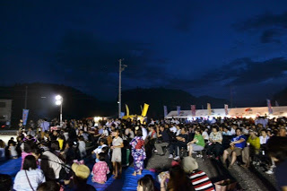 屋外の夜空の下、たくさんの人がブルーシートの上に座って花火が上がるのを待ち望んでいる様子の写真