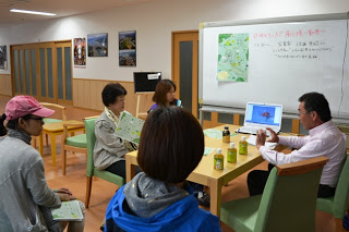 室内のテーブルを囲んで参加者の方々が座っており、関係者からアドバイスを受けている様子を写した写真