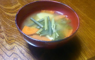 赤い縁の器に、わらびや人参、タケノコなどの具材が入った味噌汁の写真