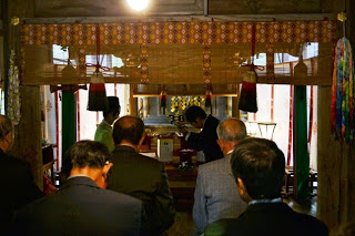 神殿の中で、スーツ姿の男性たちが祭壇に向かって深く頭を下げて祈っている写真