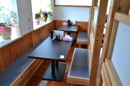 壁と仕切りに囲まれたスペースに細長いテーブルとベンチ型の座席があり、窓辺には花が飾られている落ち着いた雰囲気のベンチ席の写真