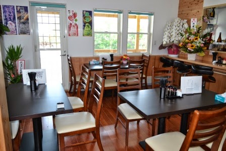 木目調の明るい店内にテーブル席が整然と並び、壁にはメニューやポスターが貼られ、入口のドアから自然光が差し込むカフェの店内の写真