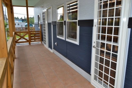 建物外側のテラス部分にタイルが敷かれ、白い格子のドアと窓が並んでおり、木の手すりで囲まれているカフェの通路の写真