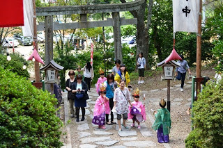 鳥居の前で色とりどりの着物を着た子どもたちが集まり、家族に付き添われながら進んでいる写真