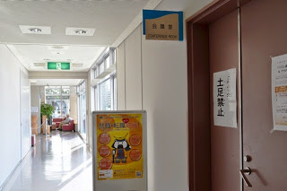 白い壁の廊下の右手に「会議室」と書かれた部屋があり、その扉には「土足禁止」と貼紙がされていて、前には黄色いイベントポスターが掲示されている写真