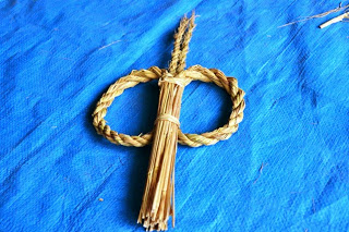 青いシートの上に、丸く編んだ縄と束ねた藁が組み合わされた小さなしめ縄が置かれている写真