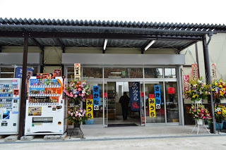 自動ドアのある店舗入口に開店祝いの花や「さかなのみうら」の看板が掲げられた様子の写真