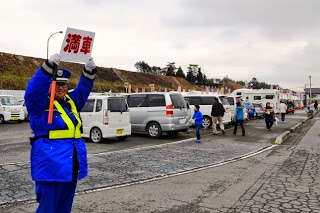 駐車場で青い制服を着た警備員が「満車」と書かれた看板を両手で高く掲げて車を誘導している様子の写真