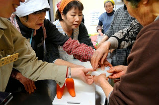 調理台の上で数人の女性たちが、右側の女性が持っているコンニャクを触っている作業中の写真