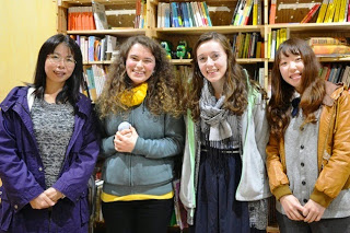 沢山の書籍が並んでいる本棚の前で、2人の女性の先生を中央に、2人の生徒が挟んで笑顔で並んで立っている写真