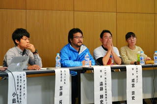 パネルディスカッションに参加する4人の登壇者が、名前の書かれた札の前に座って真剣な表情で話を聞いている写真