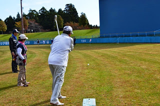 白い服を着た男性が勢いよくボールを打っているところで、他の選手たちが後ろから見守っている様子の写真