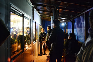 仮設食堂の外の通路で、店舗の中に入れなかった人たちが寒さの中、窓越しに明るく賑わう店内の様子を見ている写真