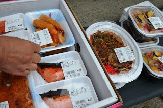 焼き鮭やフライ、焼きそばなどの数種類の総菜や弁当が並んでいる写真