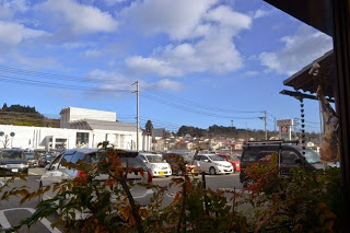 青空の下、駐車場に車が並び、小さな町並みや、遠くの建物が見える、レストランの窓際から外を眺めた風景の写真