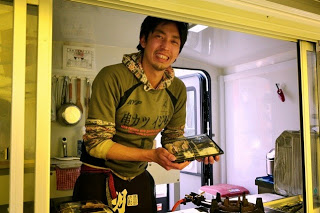 笑顔の井尻一典さんがお弁当を持っている写真