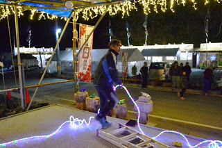 ステージの上で男性がカラフルな電飾を持って準備をしており、天井にはイルミネーションが灯っている写真