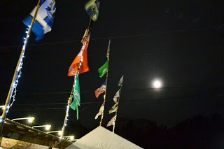 夜空に満月が浮かび、明かりに照らされた沢山の旗が風にはためいている写真