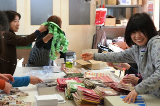 数名の女性が楽しそうに布を折りたたみながら話している作業風景の写真