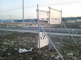 白い切り文字のきりこ看板が強風で破損し、一部が金属の支柱に残り、近くの地面にはちぎれた破片が落ちている写真