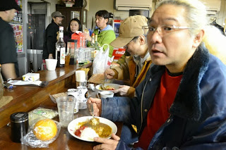 店内のカウンター席に座った人々がカレーライスを食べている様子を写した写真