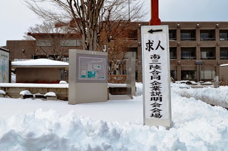 雪が積もった屋外の歩道に「求人合同企業説明会場」の案内看板が立っている風景の写真